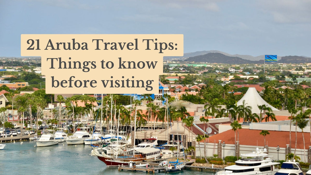 Aruba harbor with sailboats and yachts moored beside palm trees and red-roofed buildings; title text reads "21 Aruba Travel Tips: Things to know before visiting".
