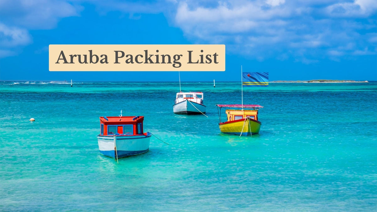 Aruba Packing List title over three colorful fishing boats anchored in turquoise Caribbean water, an Aruban flag flying behind.