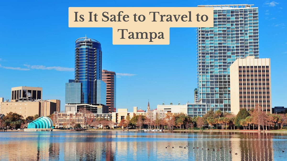 Title card "Is It Safe to Travel to Tampa" over a sunny city skyline of glass towers reflected in a calm lake with ducks.