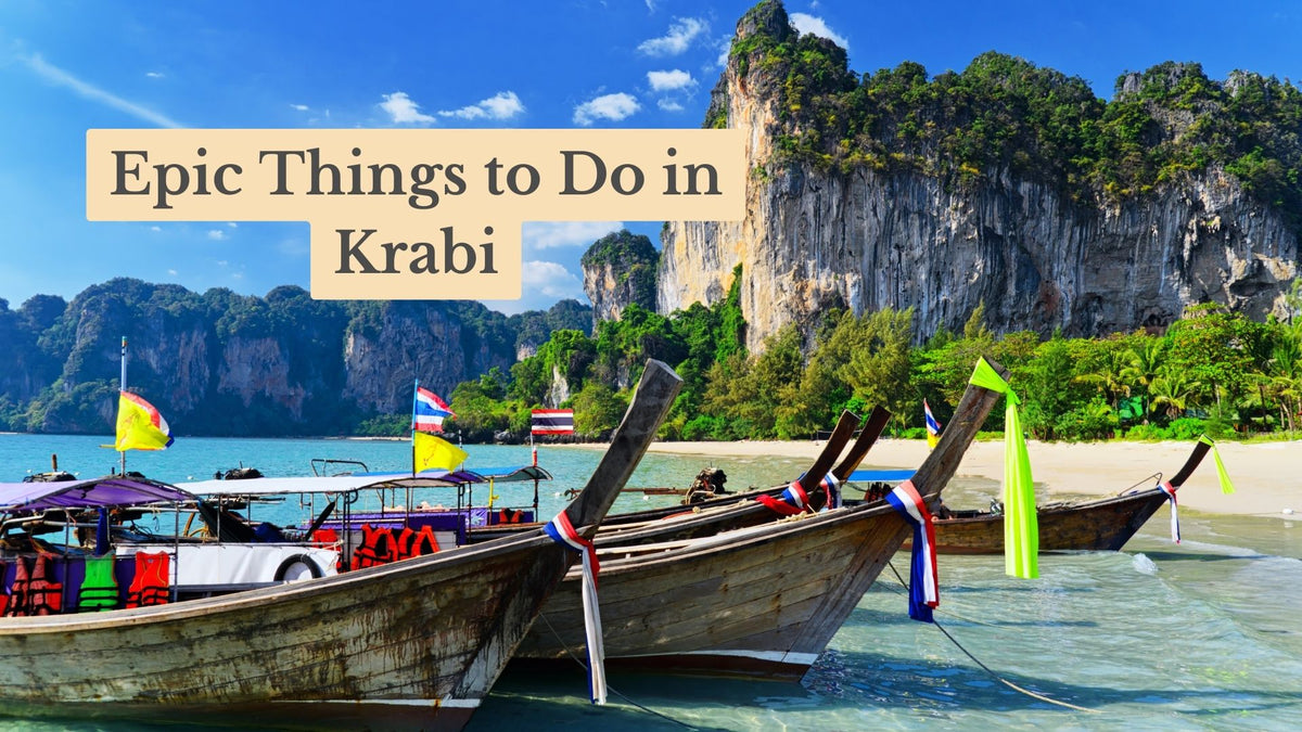 Title card "Epic Things to Do in Krabi" over wooden longtail boats with ribbons moored on a turquoise beach beneath limestone cliffs