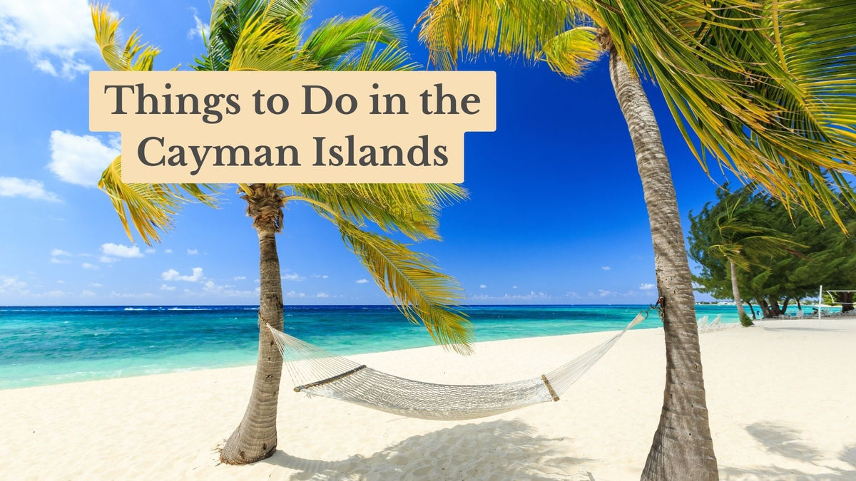 A white rope hammock hangs between two palm trees on a sandy beach by turquoise water, with the title "Things to Do in the Cayman Islands".