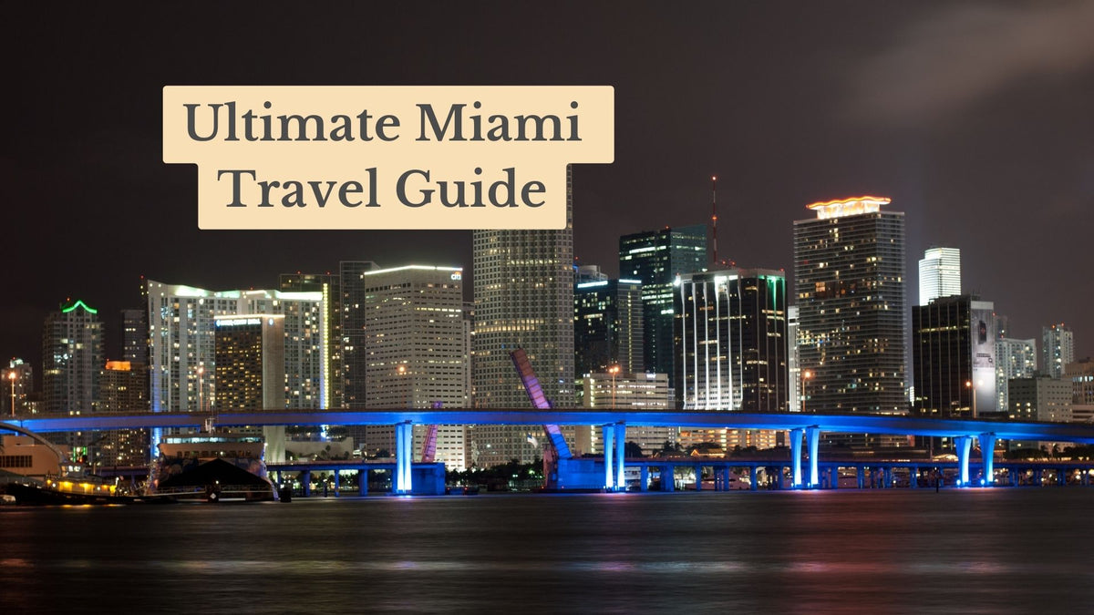 Miami skyline lit up at night over dark water, with a blue-lit bridge; title card reads "Ultimate Miami Travel Guide"